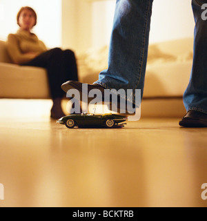 Man's foot over toy car, woman sitting in background Stock Photo