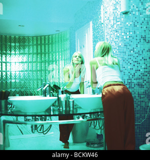 Woman leaning over sink looking at mirror in bathroom Stock Photo