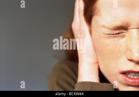 Young woman squinting eye closed, hand covering ear, close-up Stock Photo