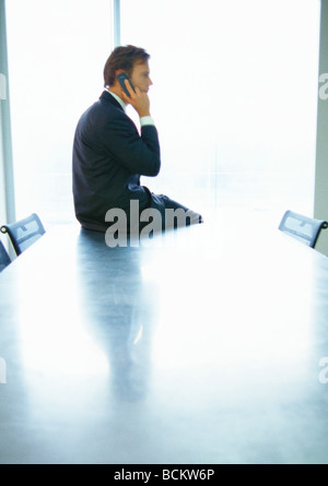 Businessman sitting on conference table, using phone Stock Photo