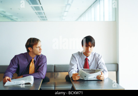 Two businessmen sitting side by side, one trying to read other's newspaper Stock Photo