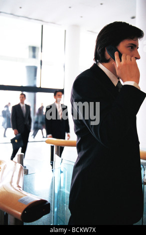 Businessman using cell phone in office lobby, side view Stock Photo