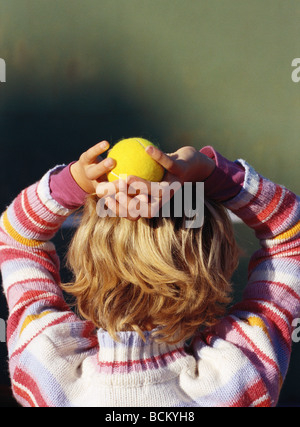 Child holding tennis ball over head, rear view