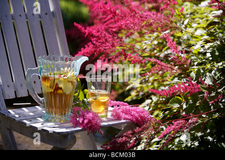 Close-up of Pimms in glass jug white wooden chair in front of pink astilbe flowers Stock Photo