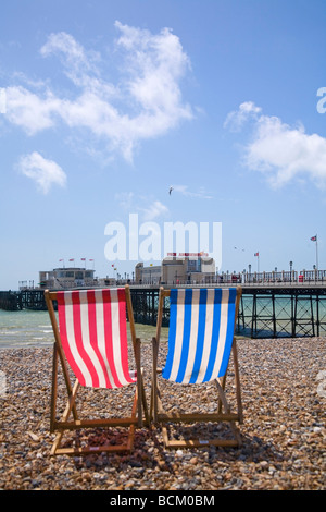 Red and Blue striped wooden deckchairs on Worthing beach facing the pier. West Sussex, UK Stock Photo