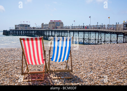 Red and Blue striped wooden deckchairs on Worthing beach facing the pier. West Sussex, UK Stock Photo