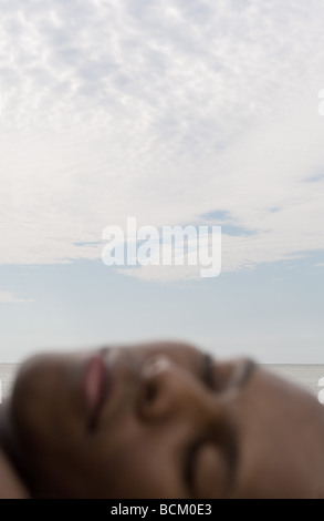 Man sleeping near ocean, blurred face in foreground, focus on sky