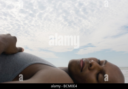 Man sleeping near ocean, focus on sky in background