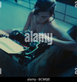 Woman sitting in bathtub, using typewriter