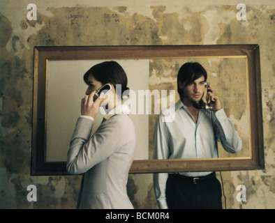 Standing on either side of picture frame, woman using cell phone and man using old-fashioned landline phone Stock Photo