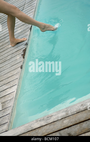 Woman standing next to swimming pool, dipping foot into water, low section Stock Photo