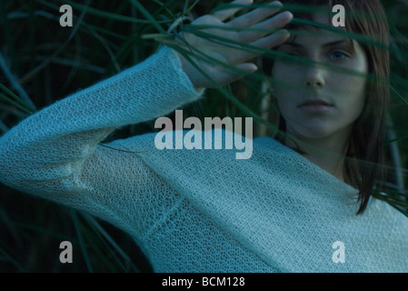 Woman moving tall grass out of face, hand raised, close-up Stock Photo