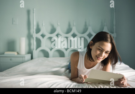 Woman lying on bed reading letter Stock Photo