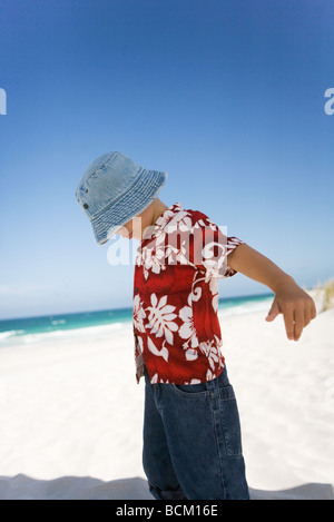 Boy standing on beach with arms out and head down