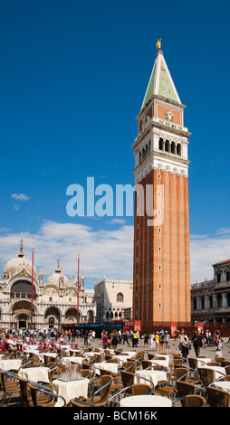 Venice St Mark's Campanile or bell tower with restaurant tables in foreground and the Basilica to the left Stock Photo