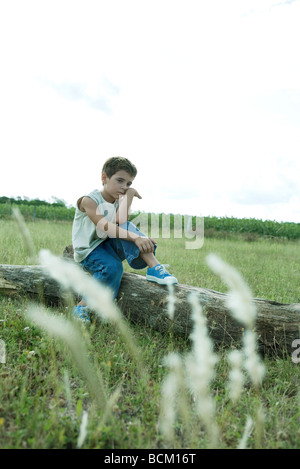Boy sitting on a tree trunk, full length