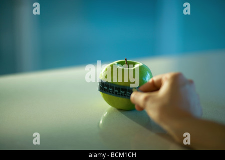 Woman holding measuring tape around apple, cropped view of hand Stock Photo