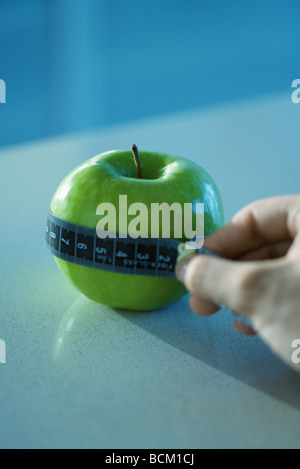 Woman holding measuring tape around apple, cropped view of hand Stock Photo