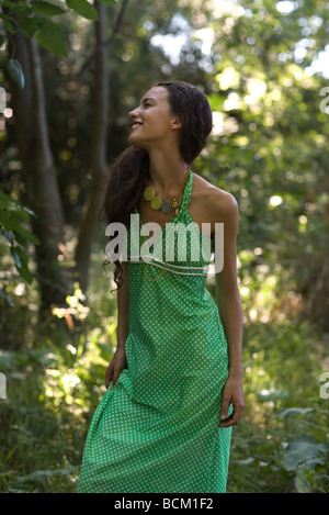 Young woman wearing sundress, standing in forest, looking away, three quarter length Stock Photo