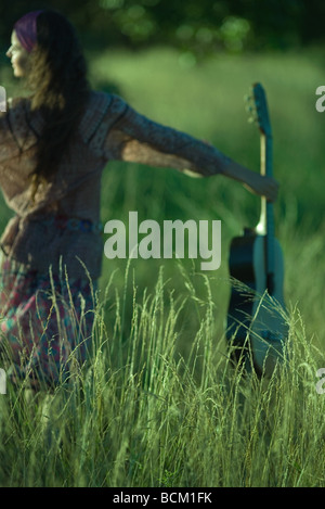 Woman walking through tall grass, holding guitar out Stock Photo