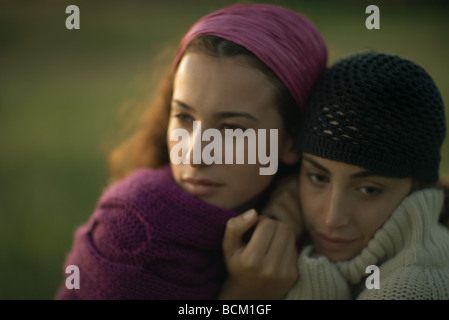 Two women huddling together, pulling sweaters up to faces, looking away, close-up Stock Photo