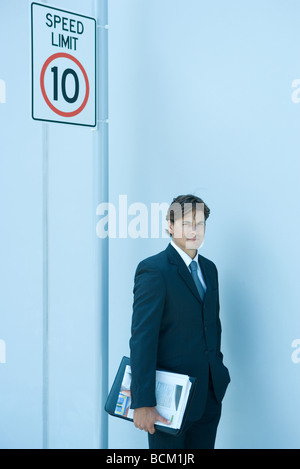 Buisnessman holding binder, standing under speed limit sign with hand in pocket Stock Photo