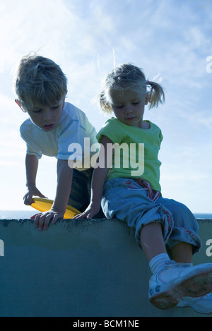 Boy and girl on wall, sky in background Stock Photo