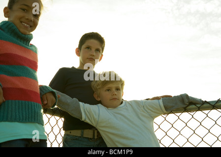 Three children leaning against chainlink fence, low angle view Stock Photo