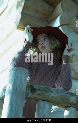 Teenage girl leaning against railing, holding hat, looking away, low angle view Stock Photo