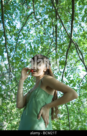 Young woman standing outdoors, eating radish, smiling at camera Stock Photo