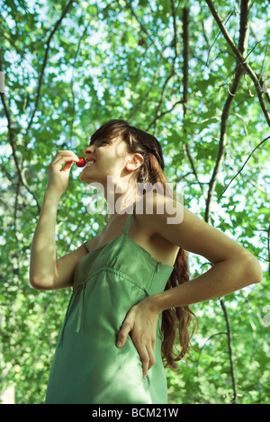 Young woman standing with hand on hip outdoors, eating radish, side view Stock Photo