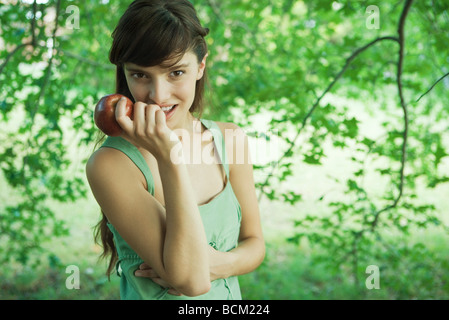 Young woman holding up apple outdoors, smiling at camera Stock Photo