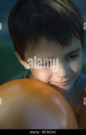 Little boy leaning cheek against balloon, smiling, looking away, portrait Stock Photo