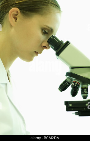 Female scientist looking through microscope, side view Stock Photo
