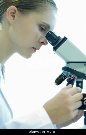 Female scientist looking through microscope, side view Stock Photo