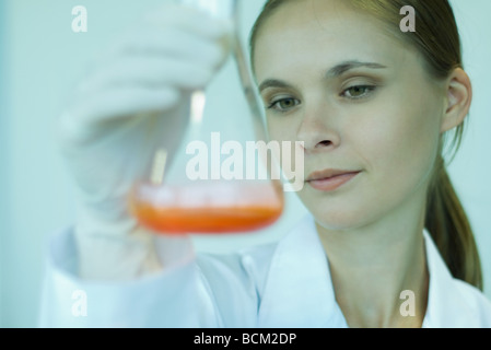 Female scientist holding up beaker with liquid inside, looking down, close-up Stock Photo