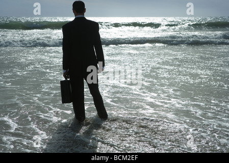Businessman walking into sea, rear view Stock Photo