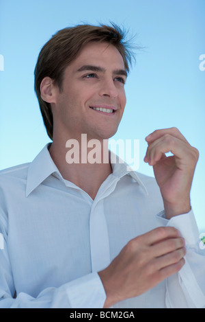 Man buttoning shirt cuff, smiling Stock Photo