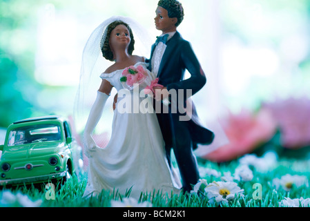 Plastic bride and groom standing in field of fake flowers, toy car in background Stock Photo