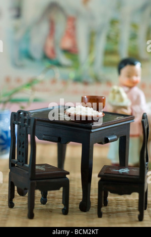 Dishes set on miniature table, doll standing in background Stock Photo