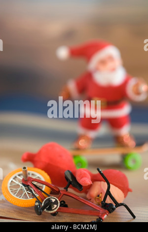 Figurine falling off toy bicycle, Santa Claus skateboarding in background Stock Photo