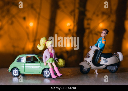 Male toy figure on moped approaching female figure leaning against toy car