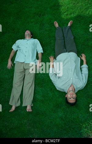 Father and adult son lying side by side on grass, high angle view Stock Photo