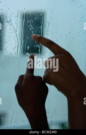 Parent and child tracing raindrops on window with fingers, cropped view of hands Stock Photo