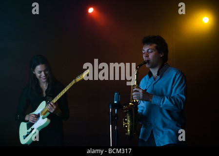 Young musicians playing electric guitar and saxophone in night club Stock Photo