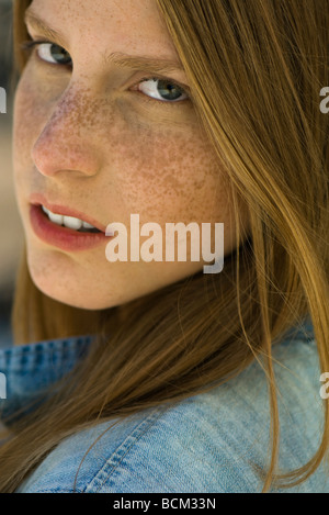 Red haired young woman looking over shoulder at camera, portrait Stock Photo