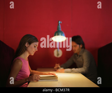Woman and man sitting in booth, woman reading in the foreground, side view Stock Photo