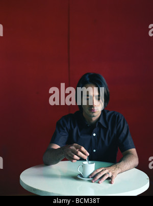 Man sitting at table with cup and saucer, stirring drink Stock Photo