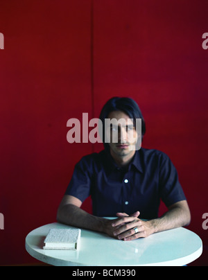 Man sitting at table with hands clasped, and book on table, looking to the side Stock Photo