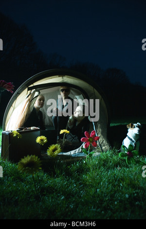 Female business associates sitting in tent at night, one using landline phone, dog sitting next to tent Stock Photo